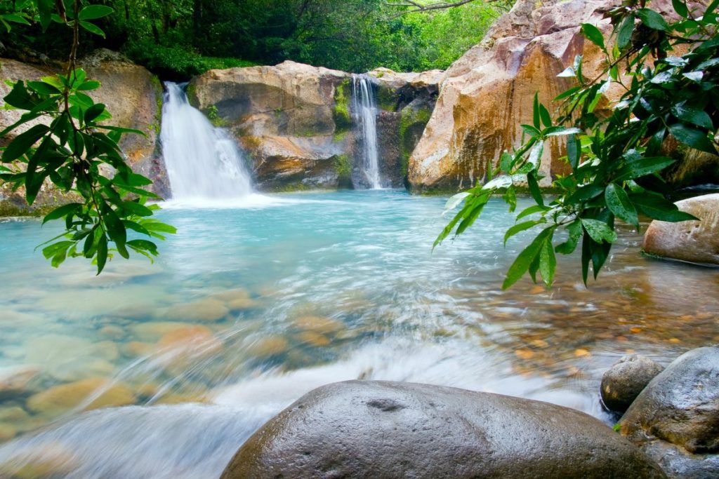 Stunning view of a small waterfall in Rincon, Puerto Rico with rocks and trees around it.